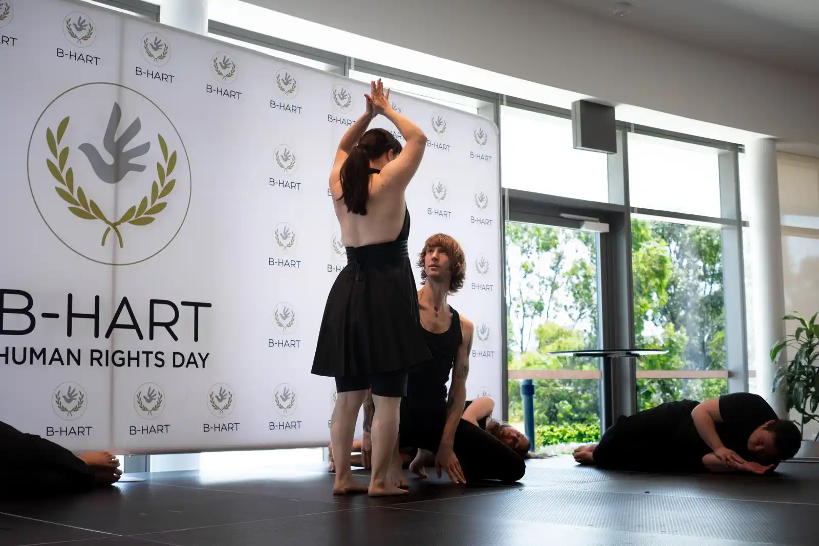 Two dancers perform in front of the B-HART Human Rights Day backdrop.