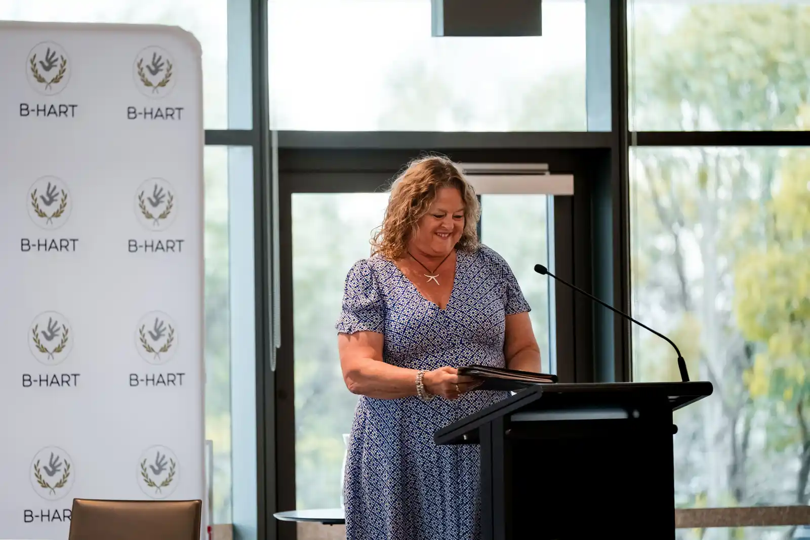 A woman speaks at a lectern in front of a B-HART banner.